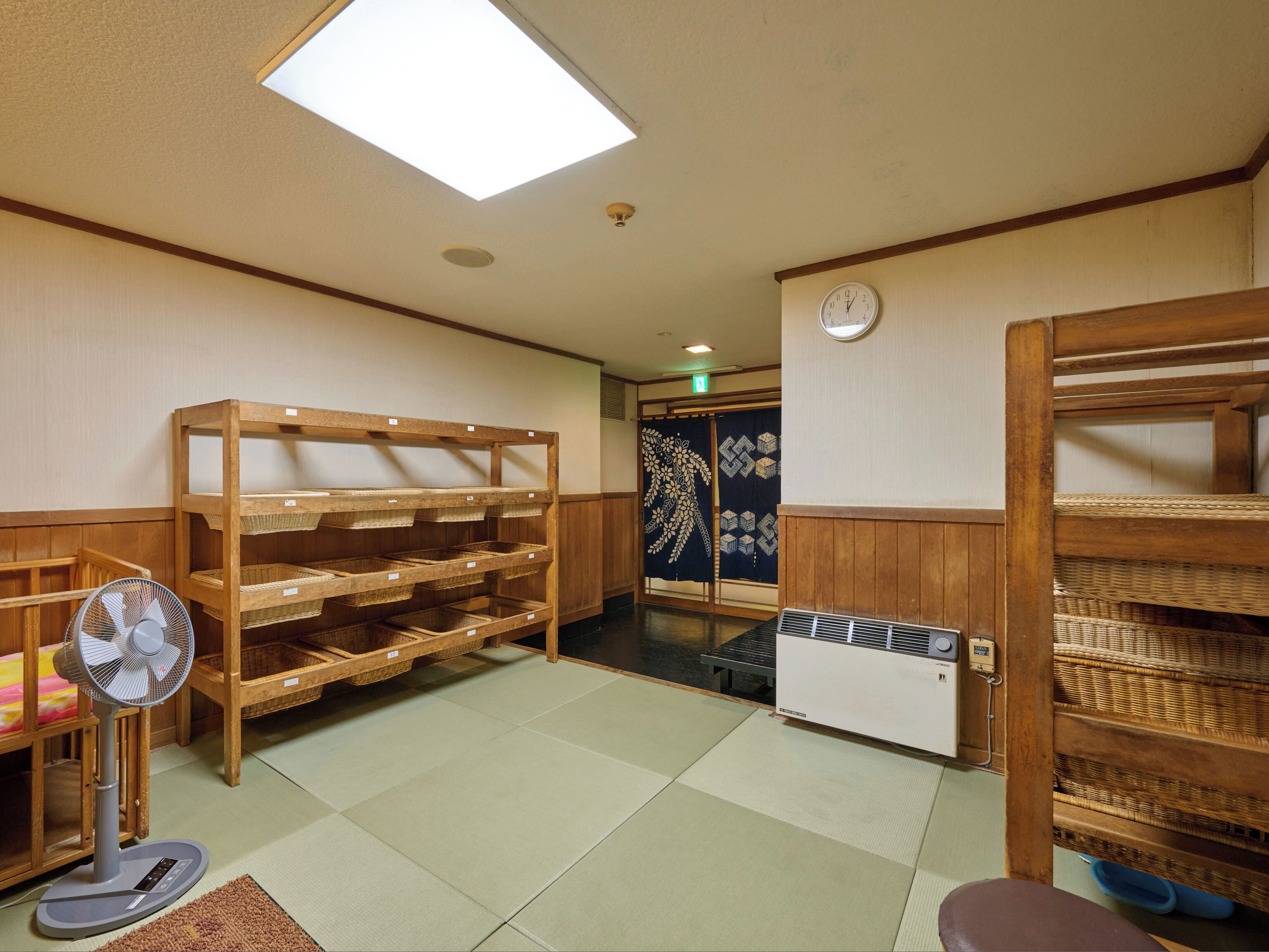 A traditional Japanese room with tatami flooring, wooden shelves, a fan, and a heater.
