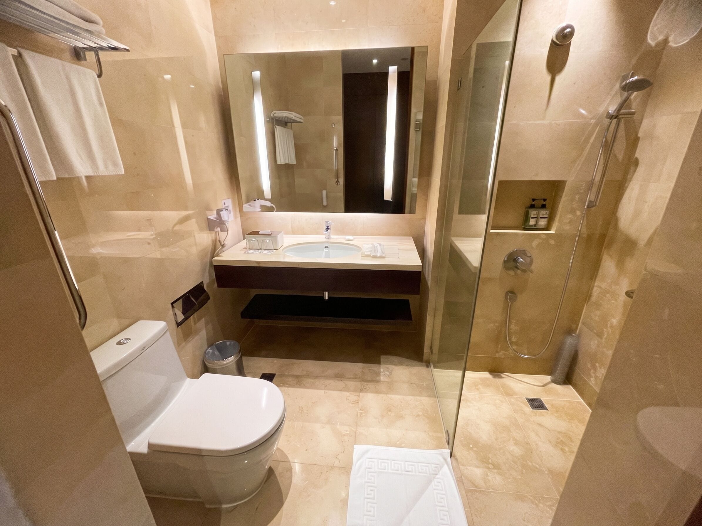 Un baño moderno con inodoro, lavamanos, espejo y ducha con mampara de vidrio.