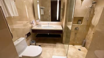 Un baño moderno con inodoro, lavamanos, espejo y ducha con mampara de vidrio.