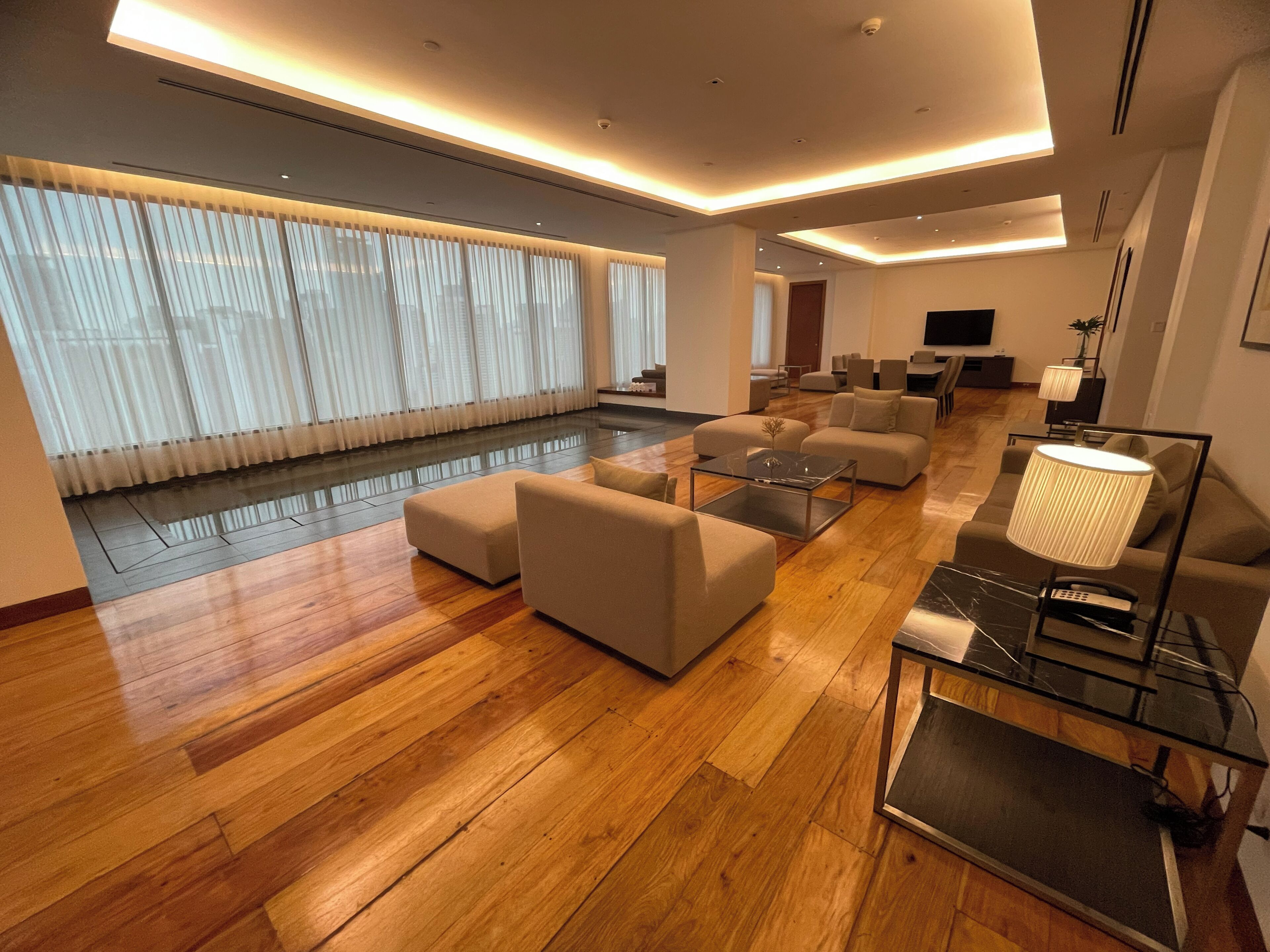 Un amplio salón con piso de madera, varios sofás, una mesa de centro de vidrio y un televisor.