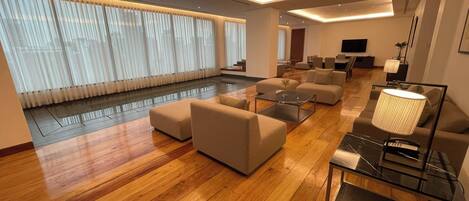 Un amplio salón con piso de madera, varios sofás, una mesa de centro de vidrio y un televisor.