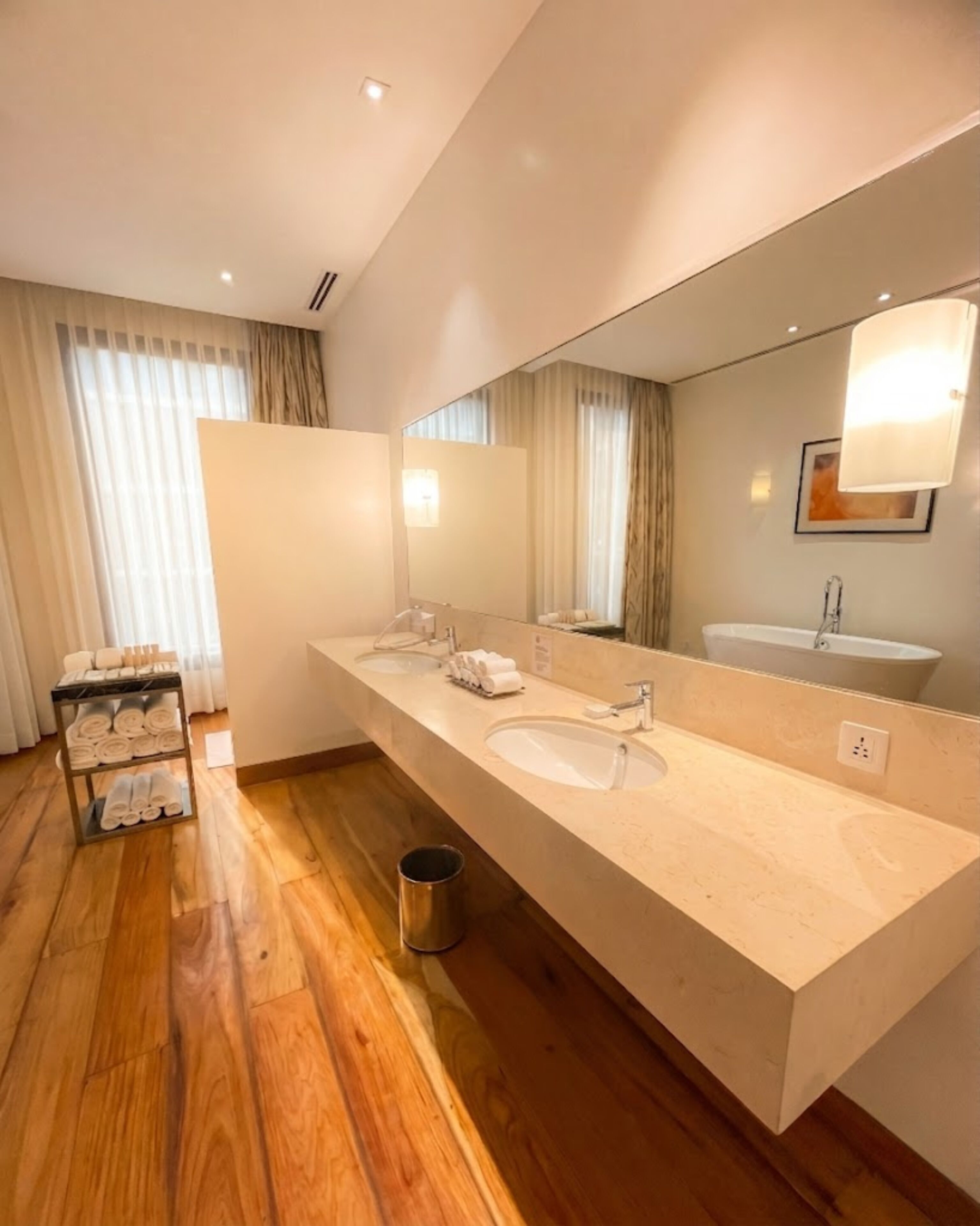 Un baño de hotel con un tocador alargado, dos lavamanos, un espejo grande y un perchero para toallas.