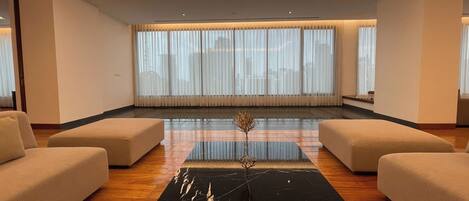 A modern living room with a black marble coffee table, beige sofas, and large windows with sheer curtains.