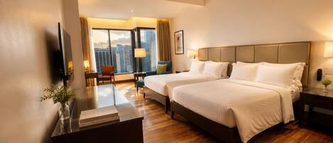 A hotel room with two beds, a desk, a chair, a TV, and a view of the cityscape.