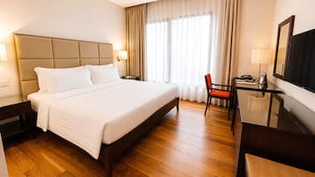 A hotel room with a large bed, a desk with a chair, a television, and a window with curtains.