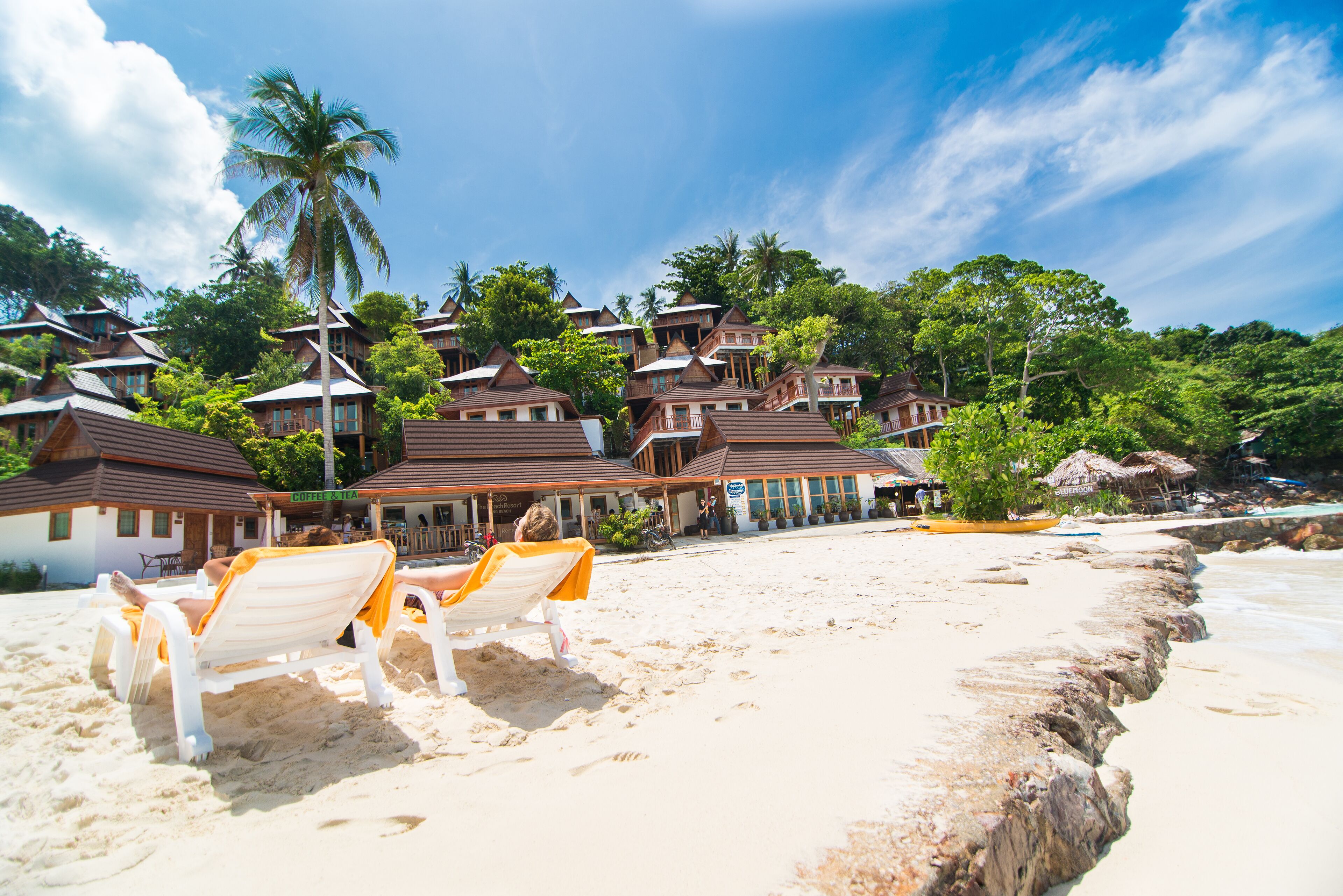 A beach resort with multiple bungalow-style buildings, a sandy beach, and palm trees.