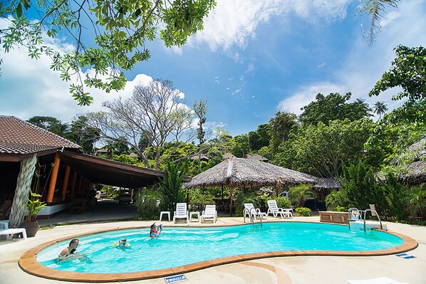 Una piscina rodeada de sillas de descanso y sombrillas de paja, en un entorno tropical.