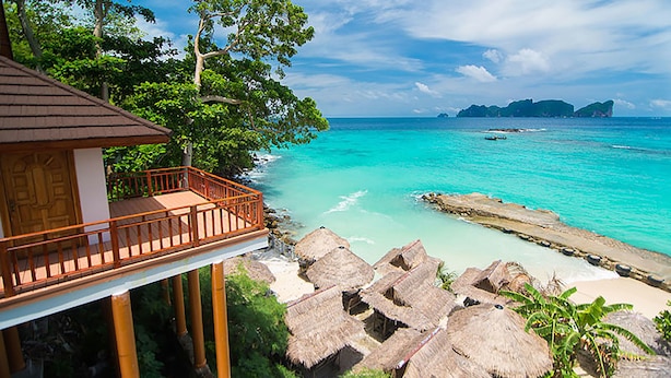 Un complexe hôtelier en bord de mer doté d’une terrasse en bois, de bungalows aux toits de chaume et offrant une vue dégagée sur la mer turquoise et les îles lointaines.