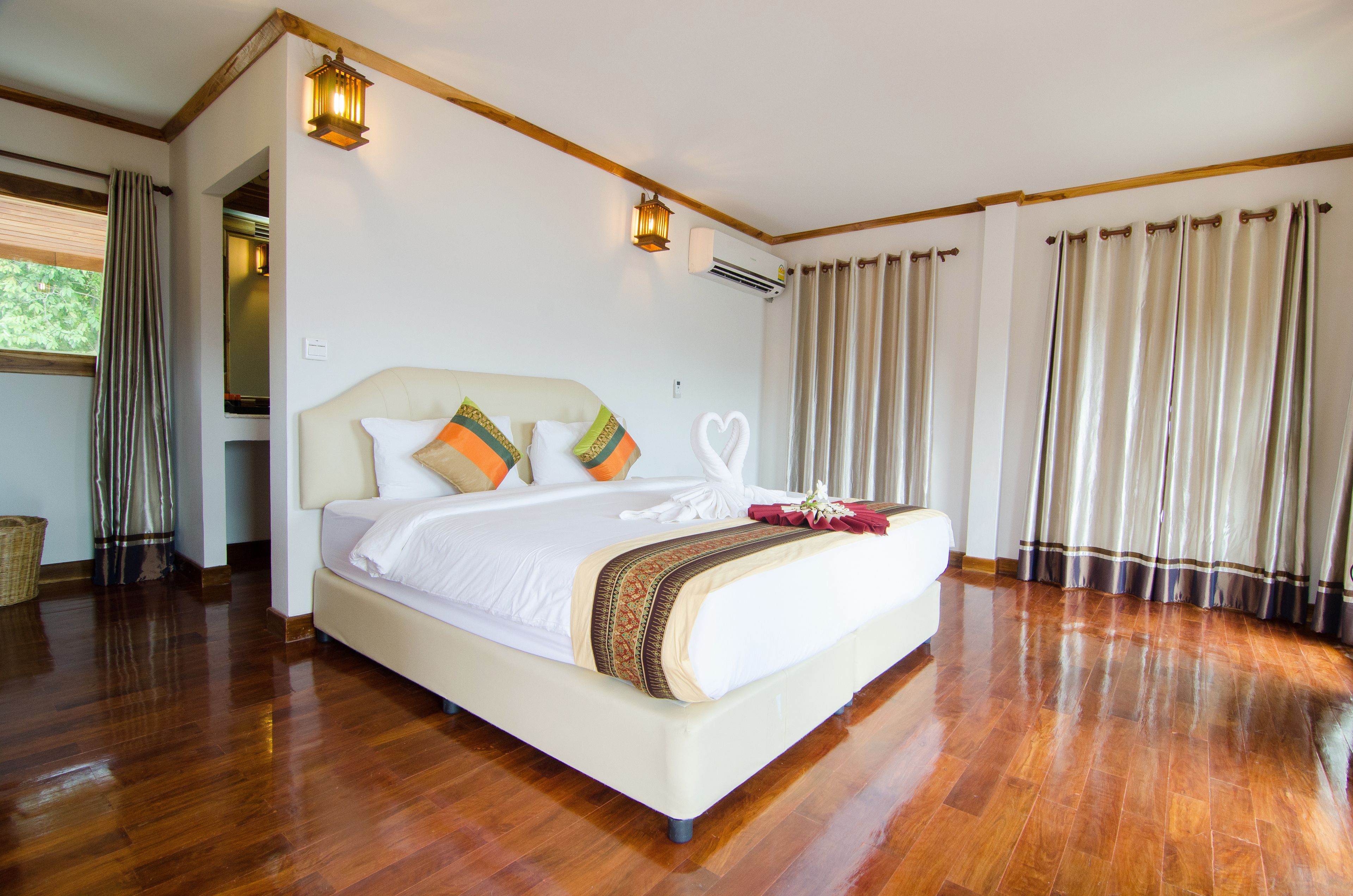 Une chambre spacieuse avec un grand lit, un plancher en bois et une vue sur l’extérieur.