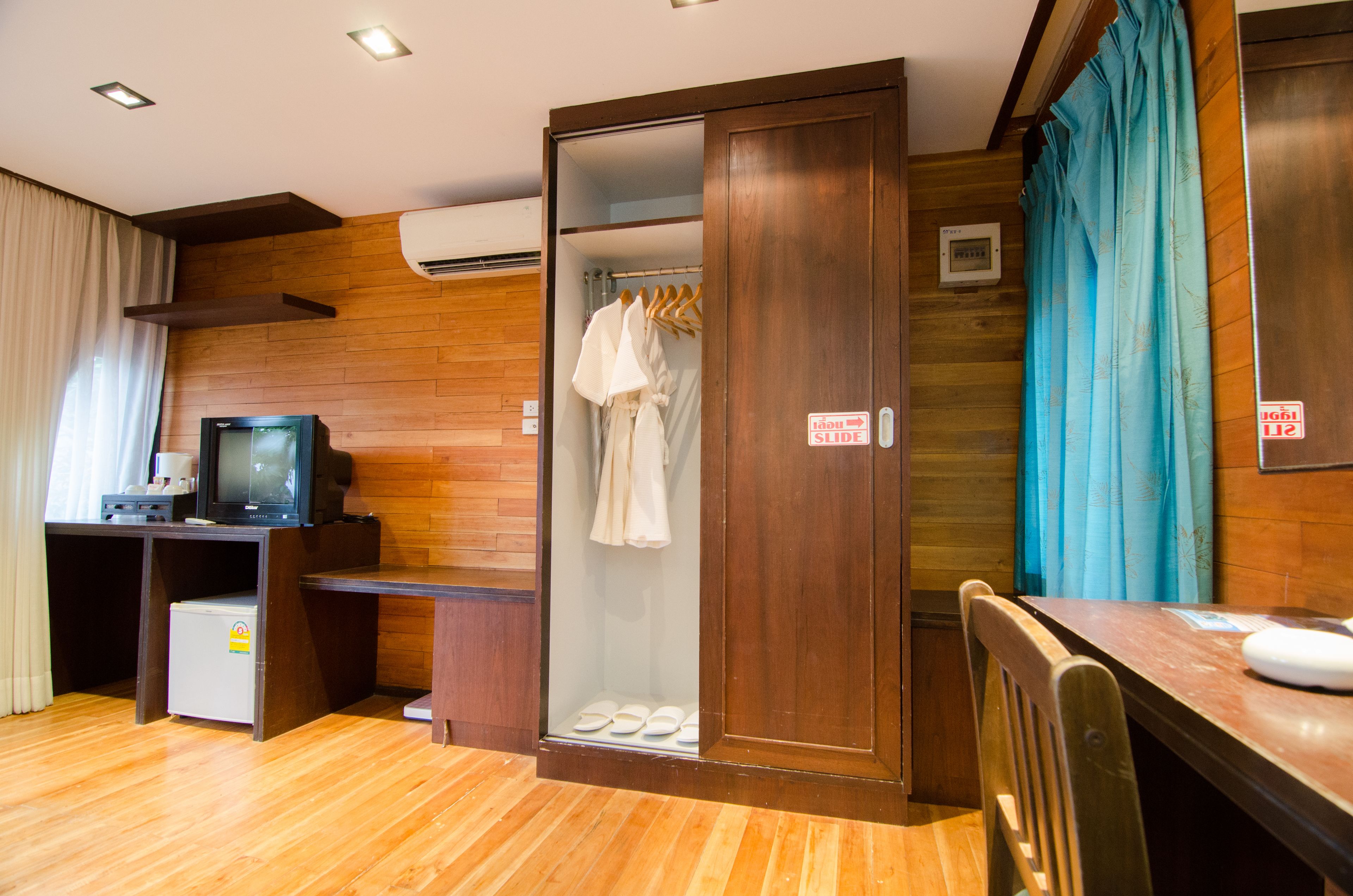 Quarto de hotel com piso de madeira, uma escrivaninha com televisão, guarda-roupa e área de chuveiro.