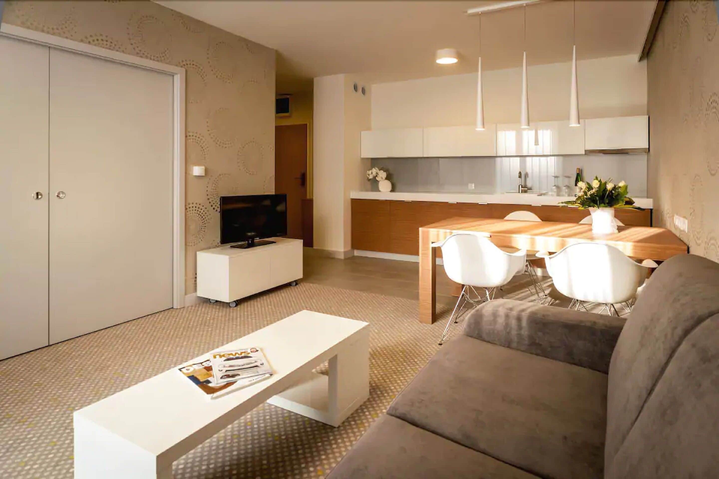 Ein modernes Wohnzimmer mit einer Couch, einem Couchtisch, einem Fernseher und einem Essbereich mit Stühlen und einem Tisch.