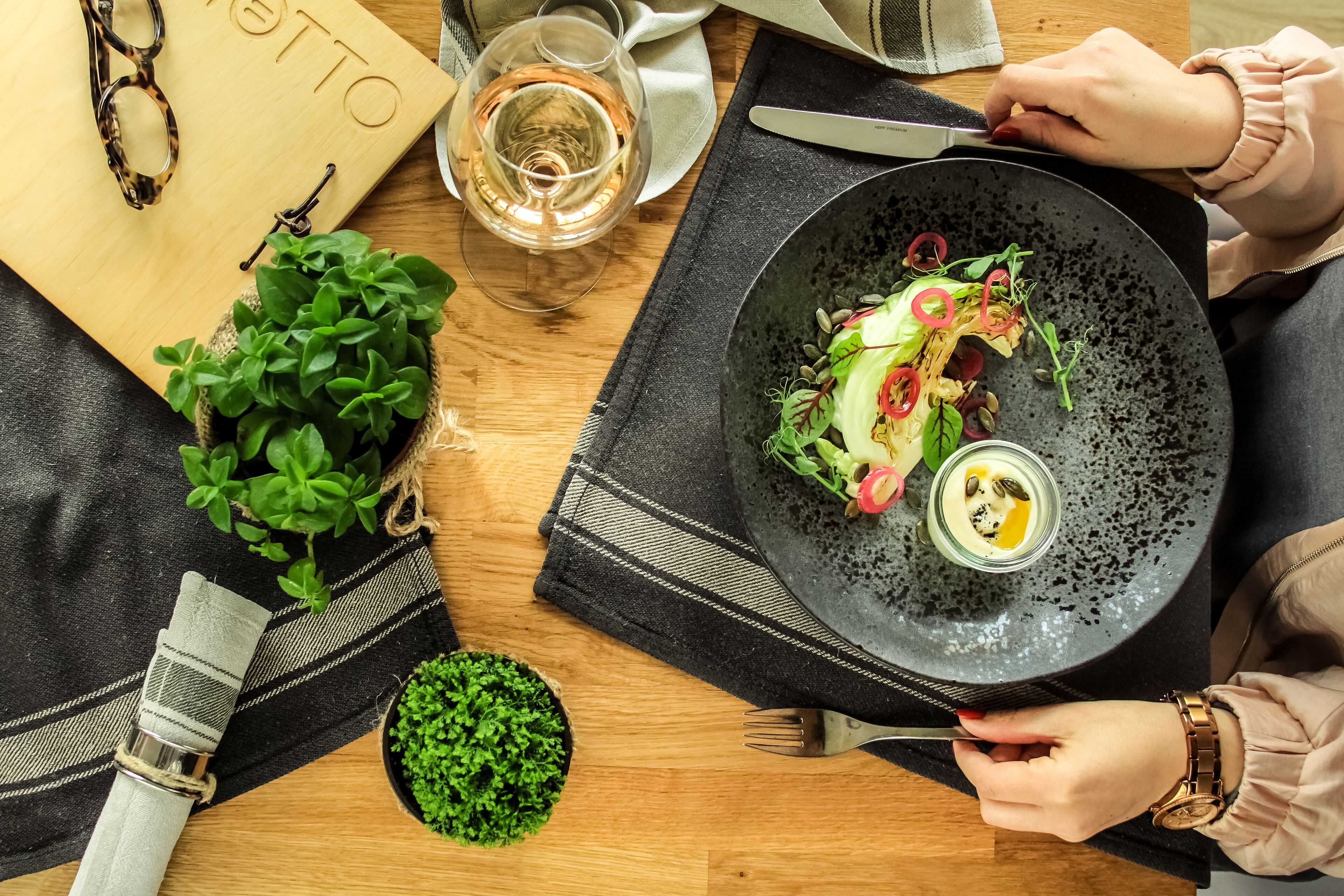 A dining table with a plate of salad, a glass of wine, and a pair of glasses.