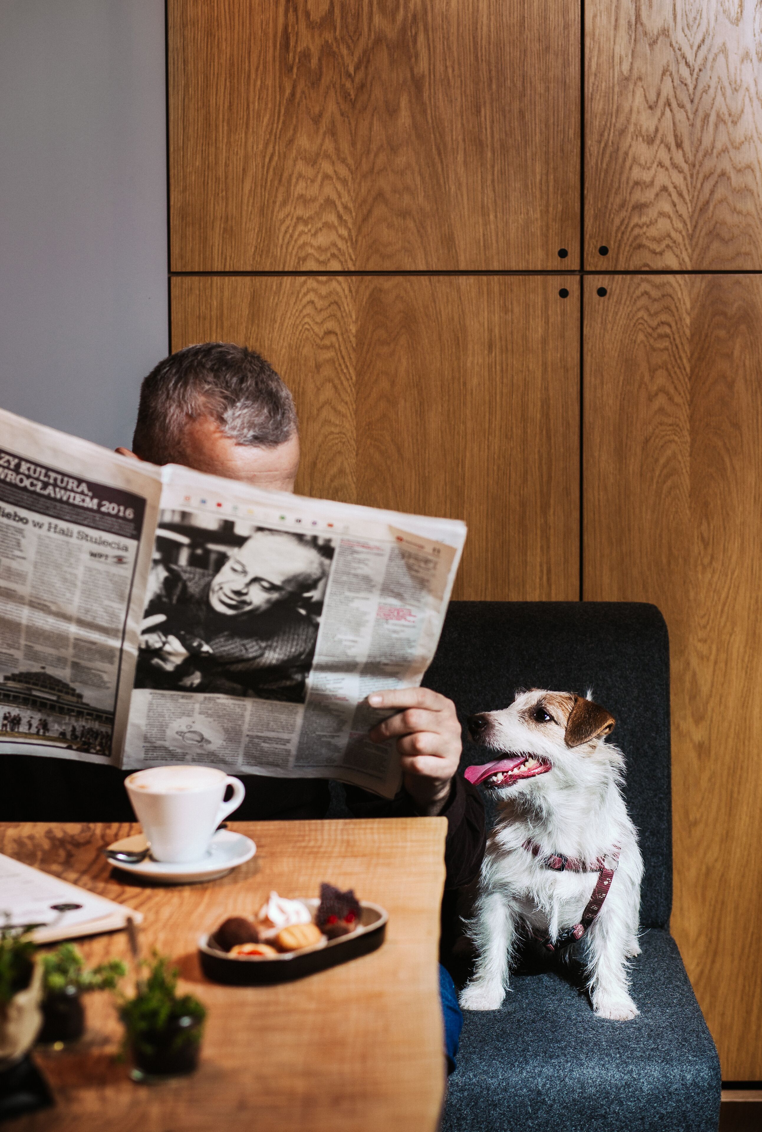 Une personne est assise à une table, un journal ouvert devant elle, et un chien est assis à ses côtés.
