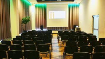Un salón de conferencias con hileras de sillas, un atril y una pantalla de proyector.