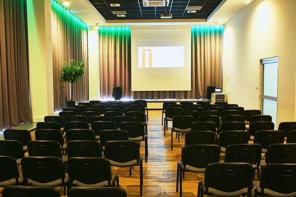 A conference room with rows of chairs, a podium, and a projector screen.