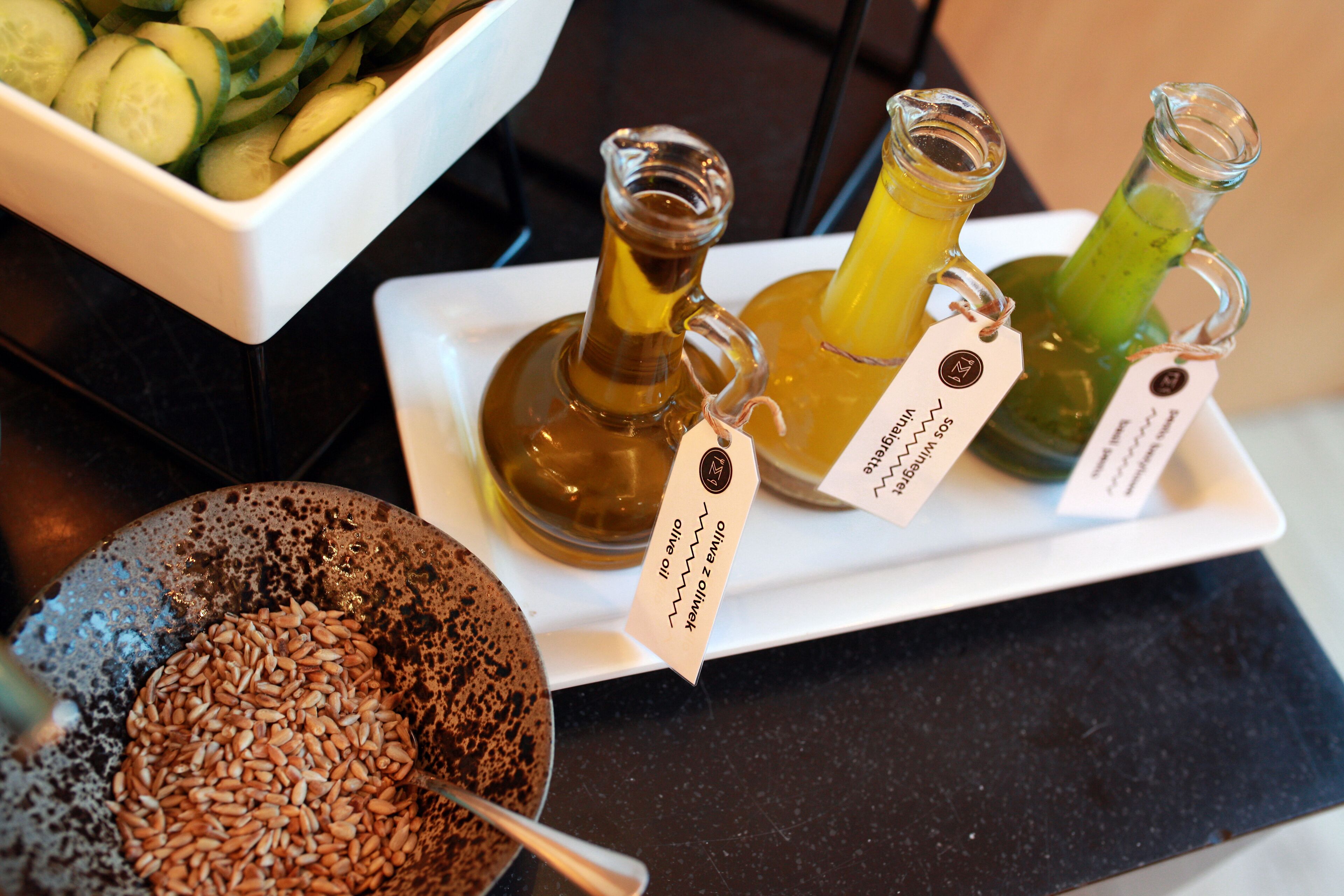 A tray with three labeled bottles of olive oil and a bowl of sliced cucumbers.