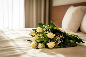 A bouquet of white roses and greenery on a bed in a hotel room.