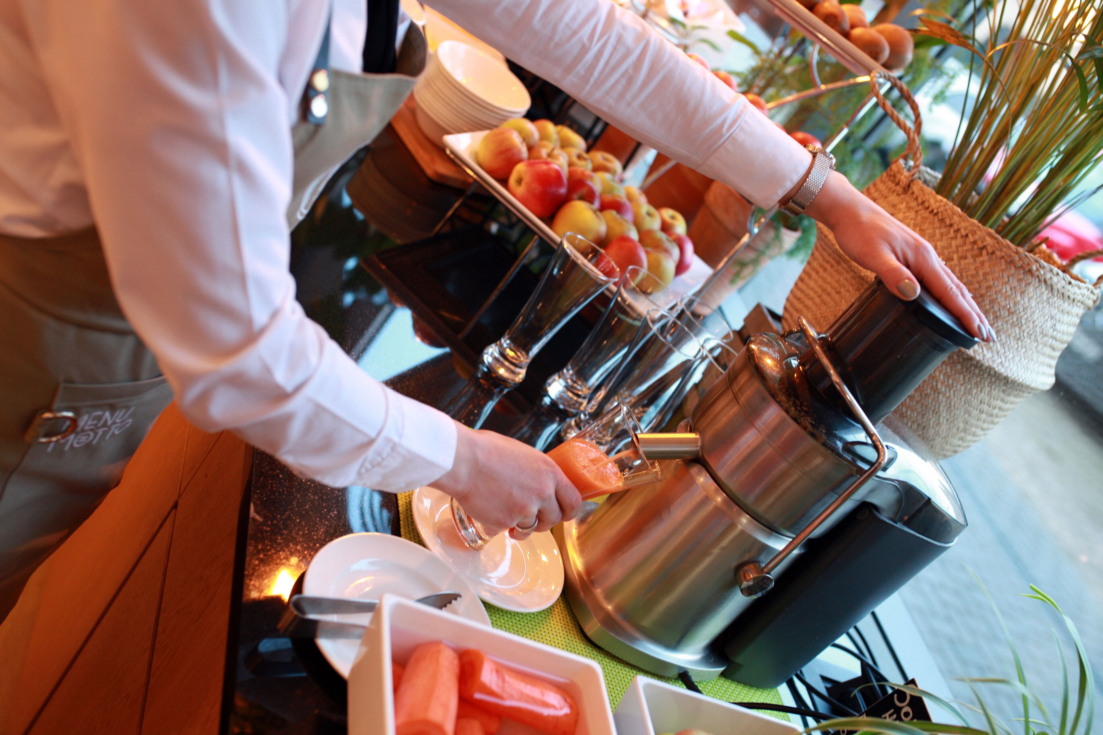A buffet setup with a variety of fruits, a beverage dispenser, and a plate of vegetables.