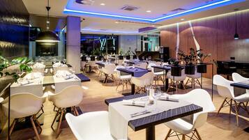 A modern restaurant with white chairs, tables, and blue lighting accents.