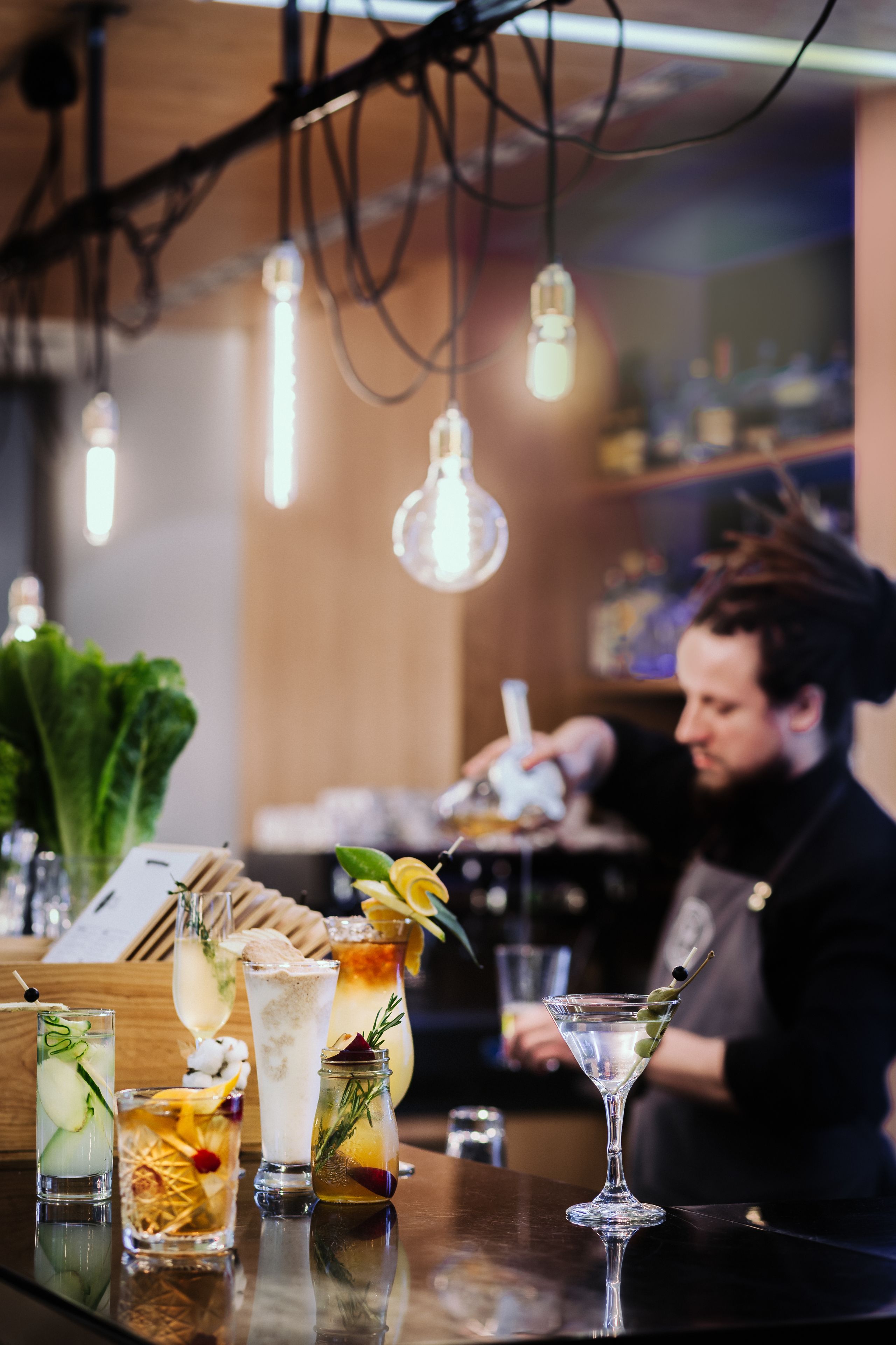 A bar with various drinks, a bartender, and hanging lights.