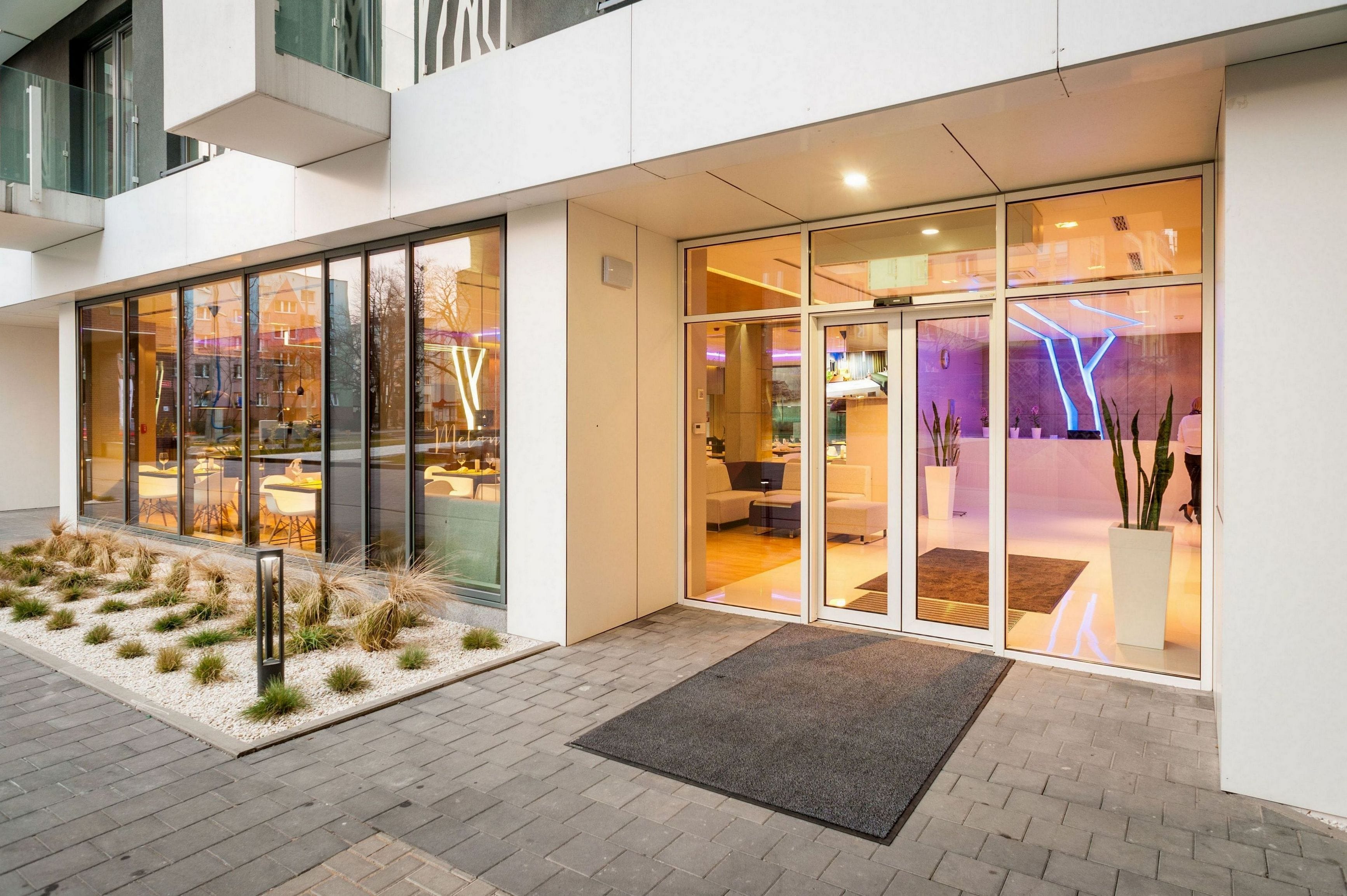 A modern hotel entrance with glass doors, a welcoming outdoor seating area, and a visible interior with contemporary furnishings.