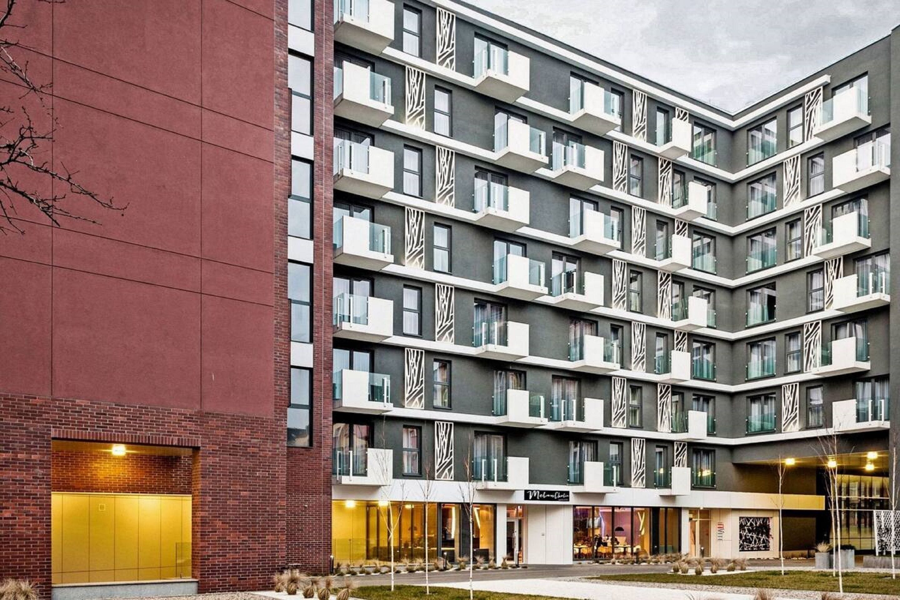 A multi-story hotel with a modern design, featuring balconies, large windows, and a brick facade.