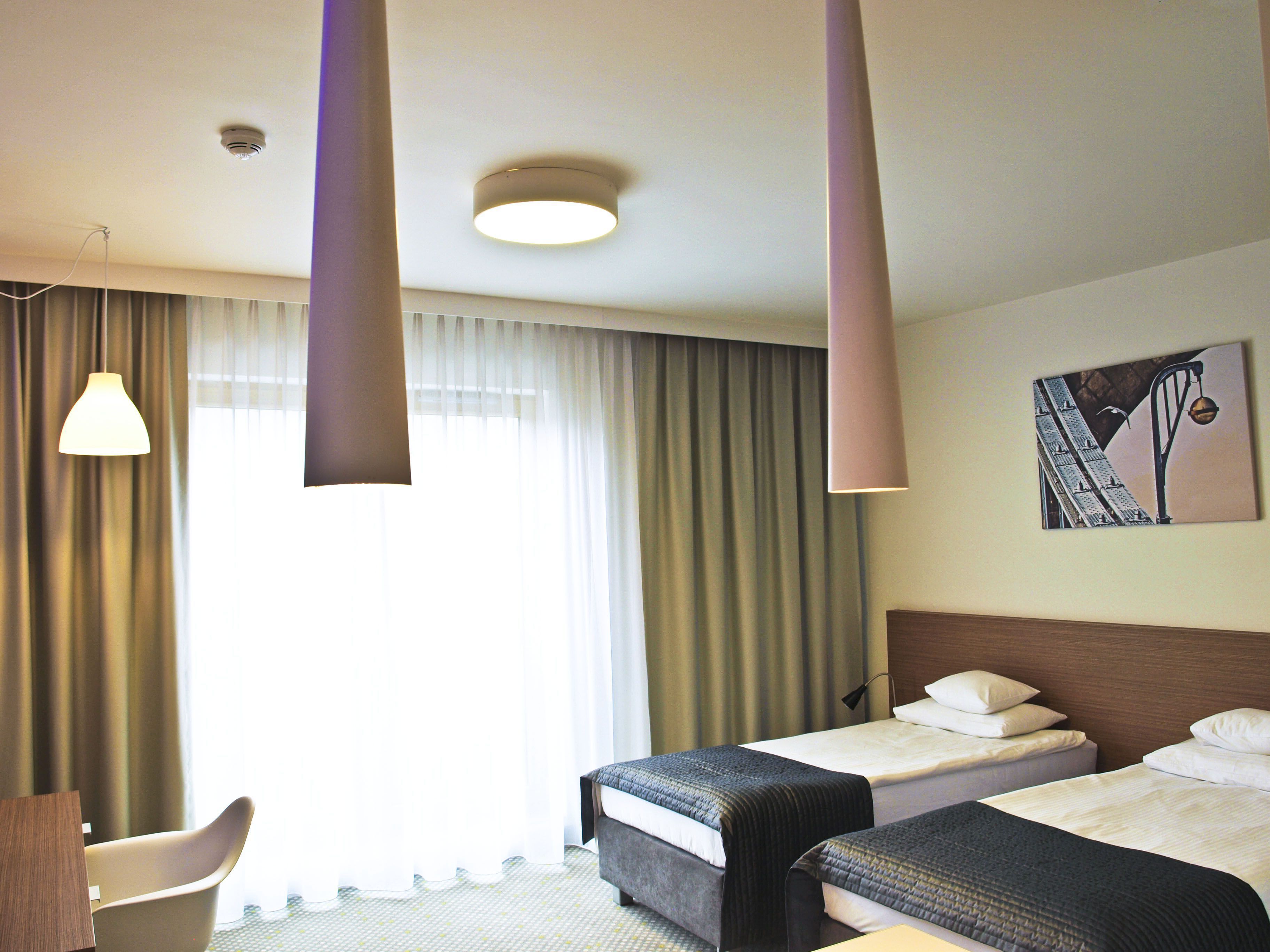 A hotel room with two beds, a desk, and a large window with curtains.