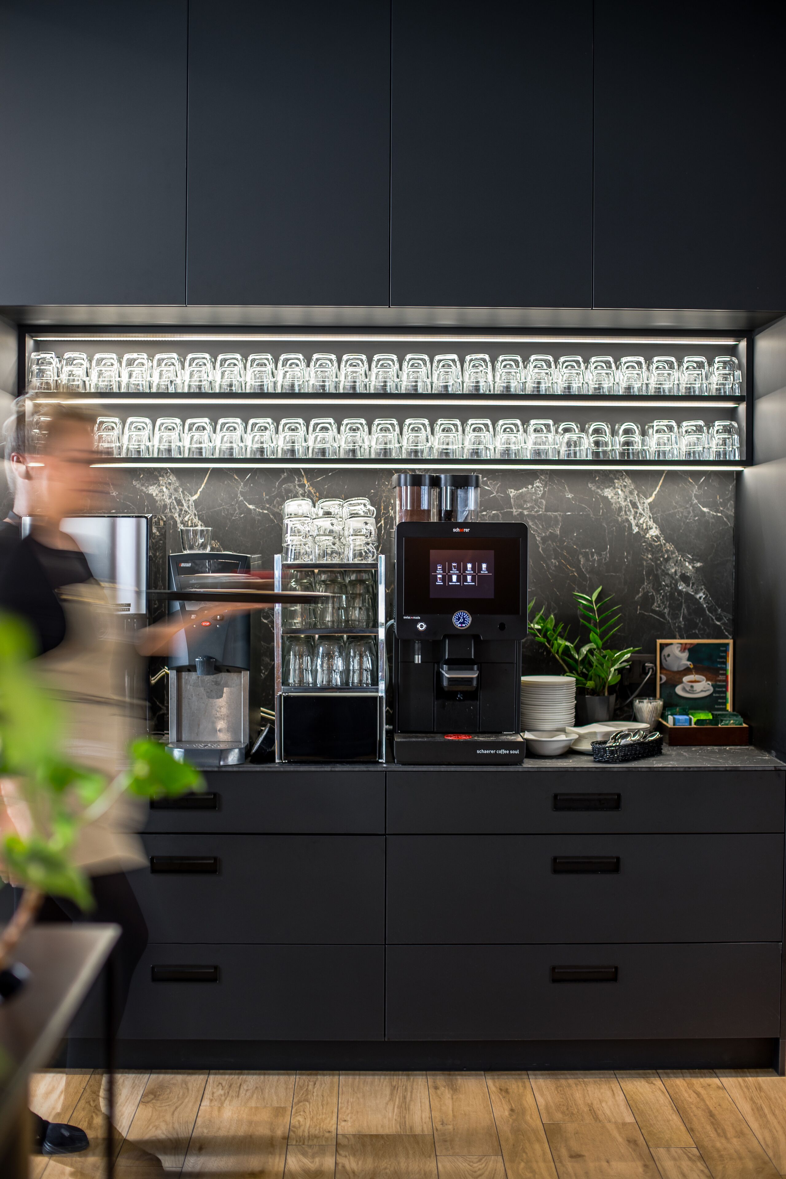 A modern bar area with a coffee machine, glassware, and a digital menu display.