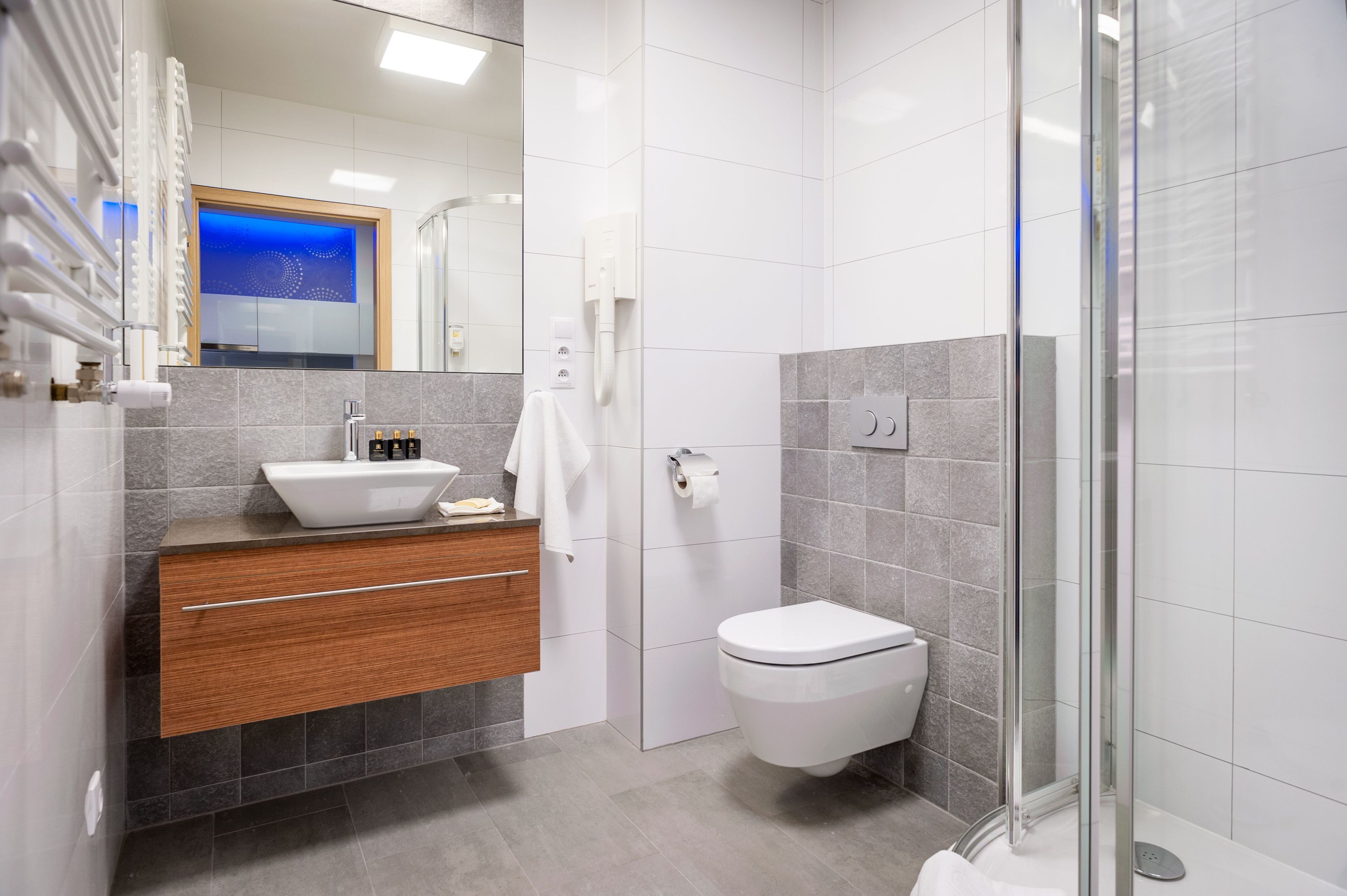 Een moderne badkamer met een wit wastafel, houten opbergmeubel, toilet en een douchecabine van glas.