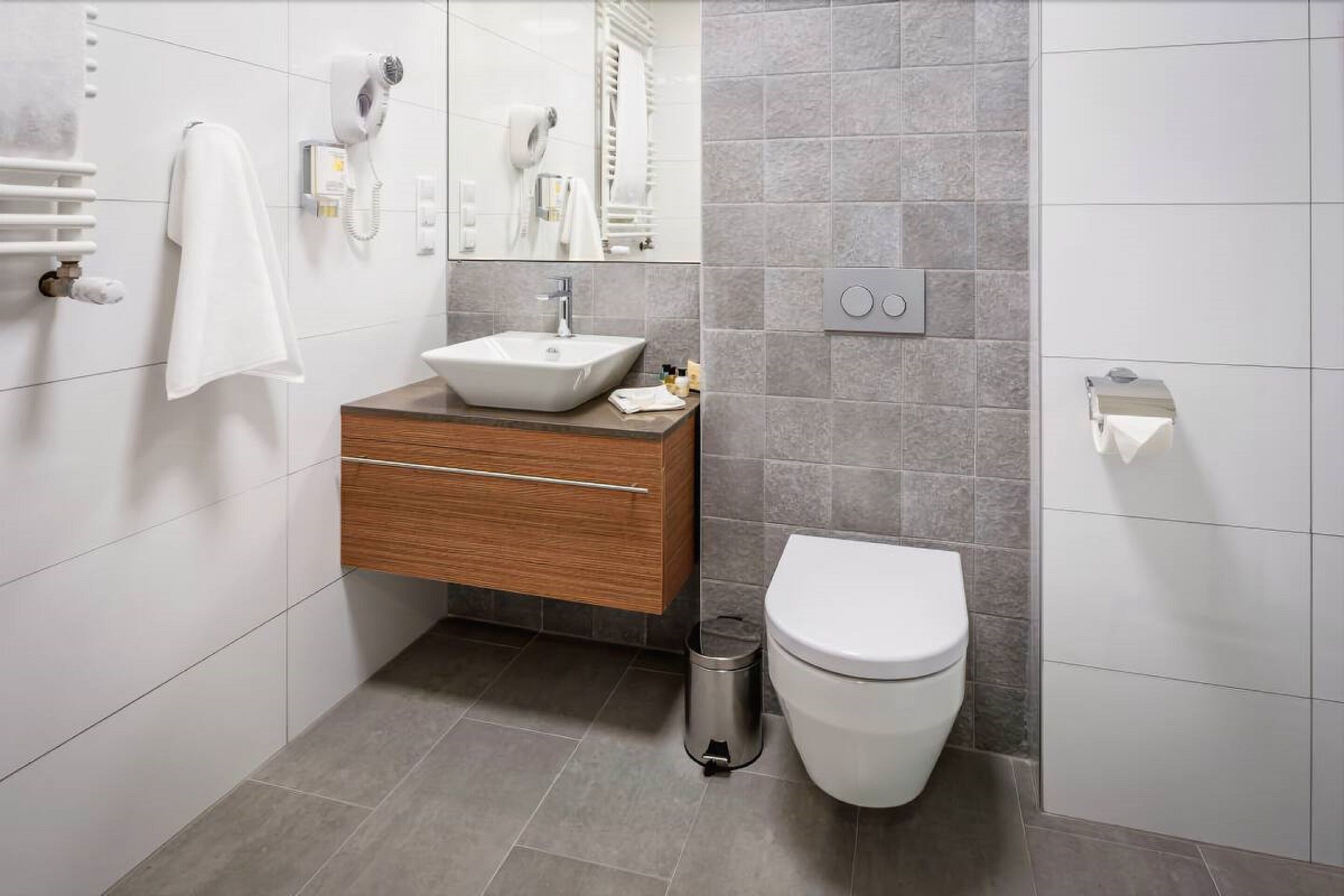 A modern bathroom with a white sink, wooden vanity, and a white toilet.
