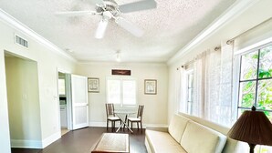 A spacious living room with a high ceiling, a ceiling fan, a sofa, a coffee table, and a dining table with chairs.