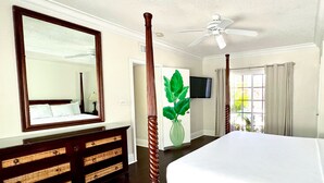 A bedroom with a large bed, a wooden dresser, a mirror, a ceiling fan, and a television.