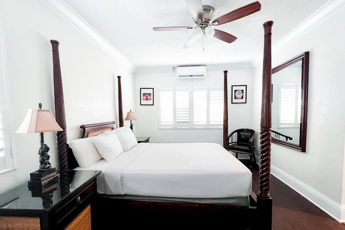 A four-poster bed with a ceiling fan, a bedside table with a lamp, and a large mirror on the wall.