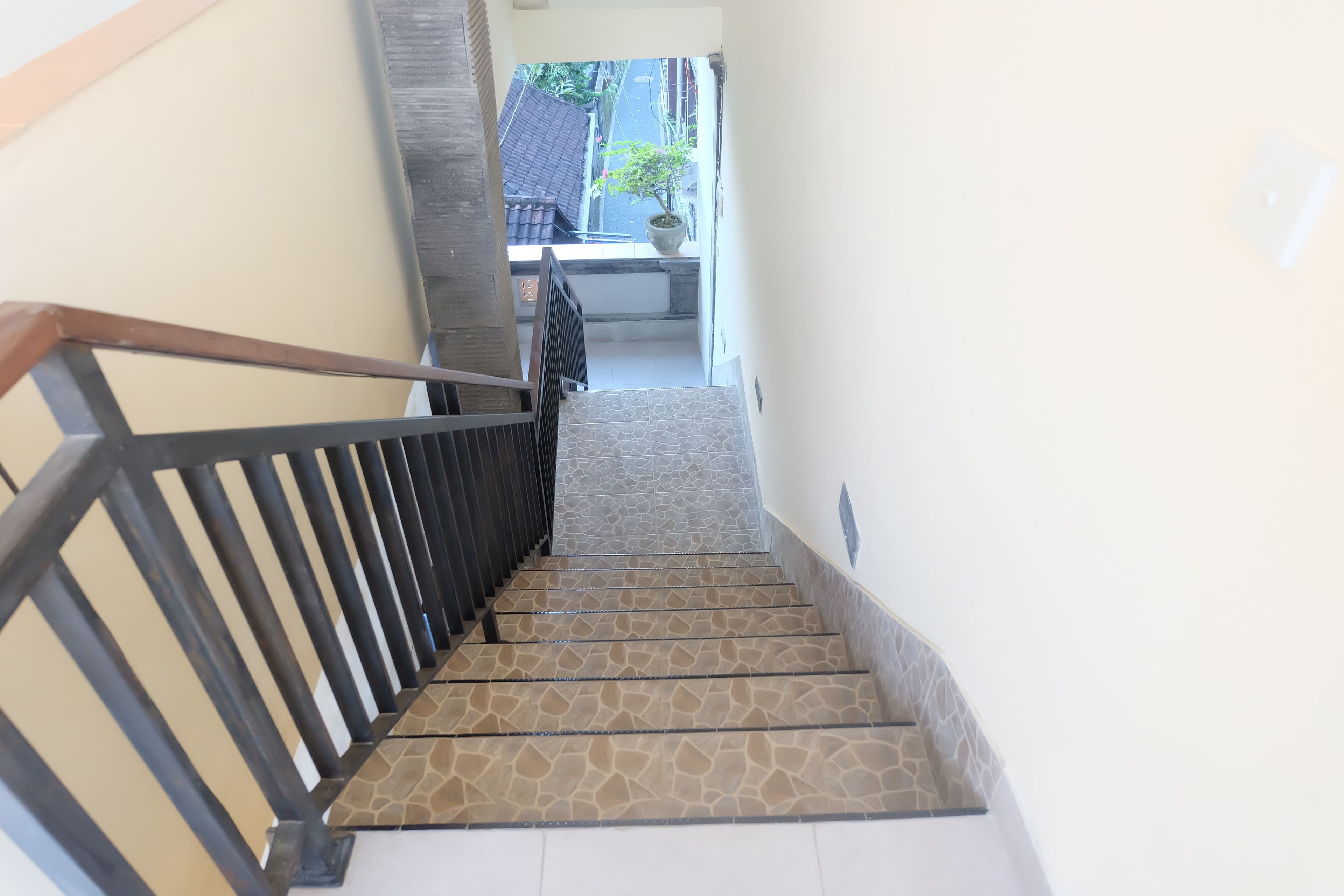 A staircase with a patterned floor and black railing, leading to a landing with a potted plant and a tiled wall.