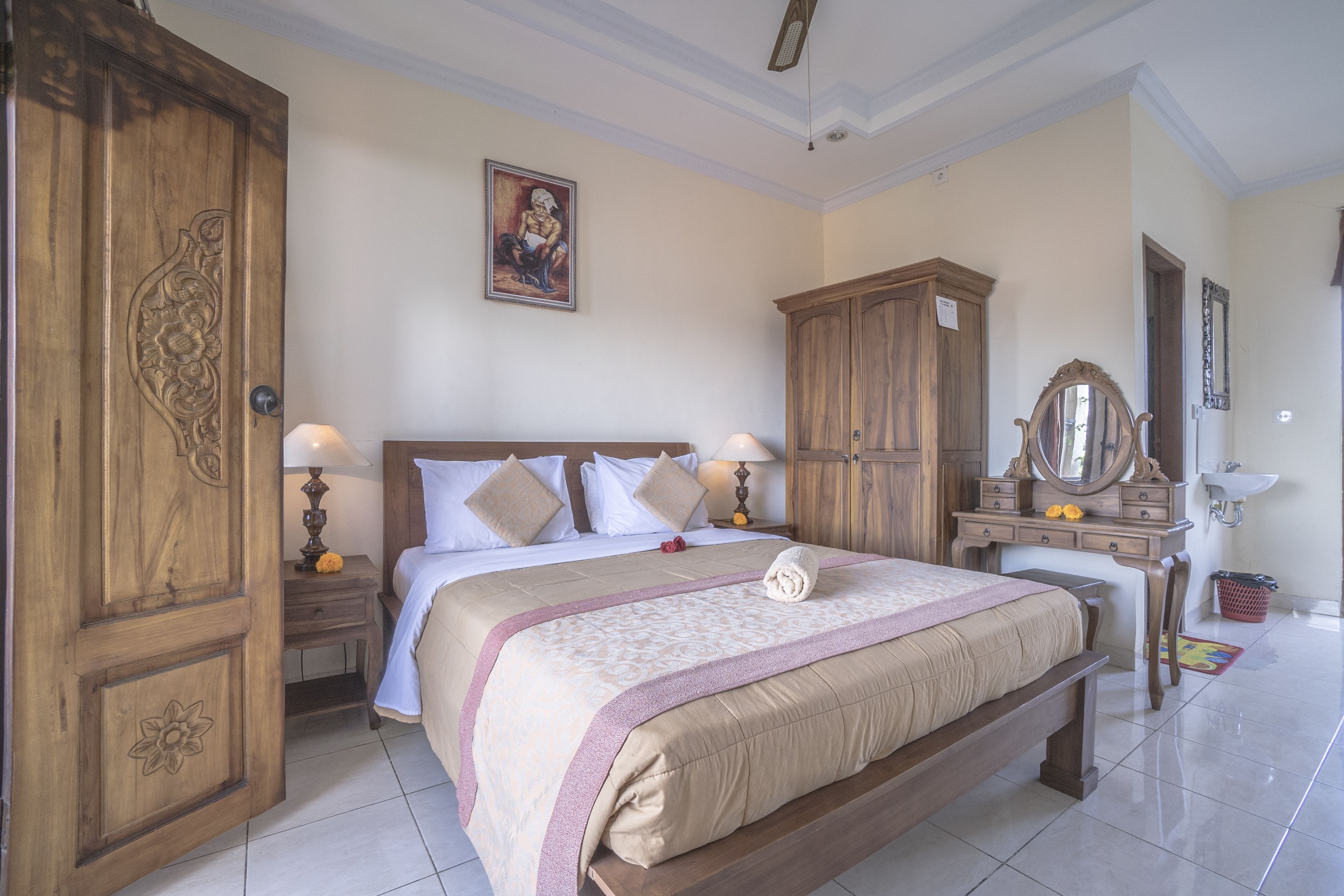 A bedroom with a large bed, wooden wardrobe, bedside tables, a mirror, and a painting on the wall.