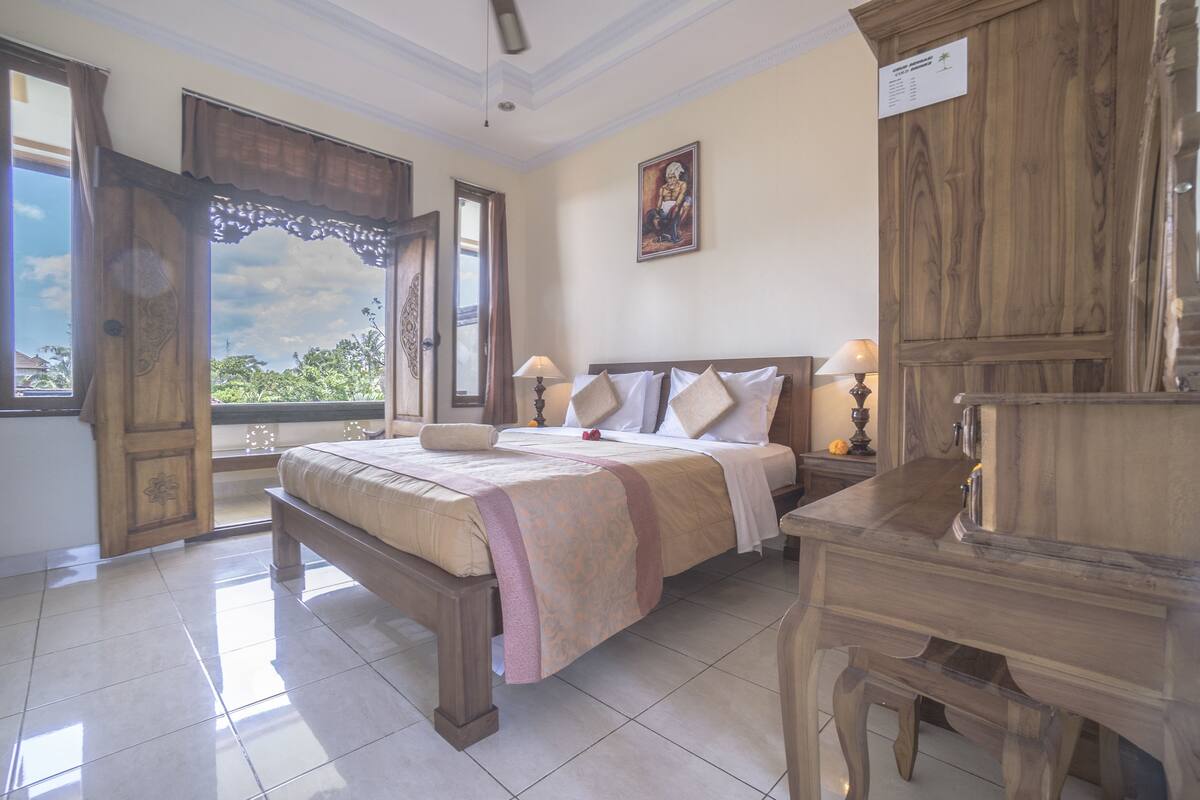 A bedroom with a bed, a wooden nightstand, a desk, and a window with curtains.