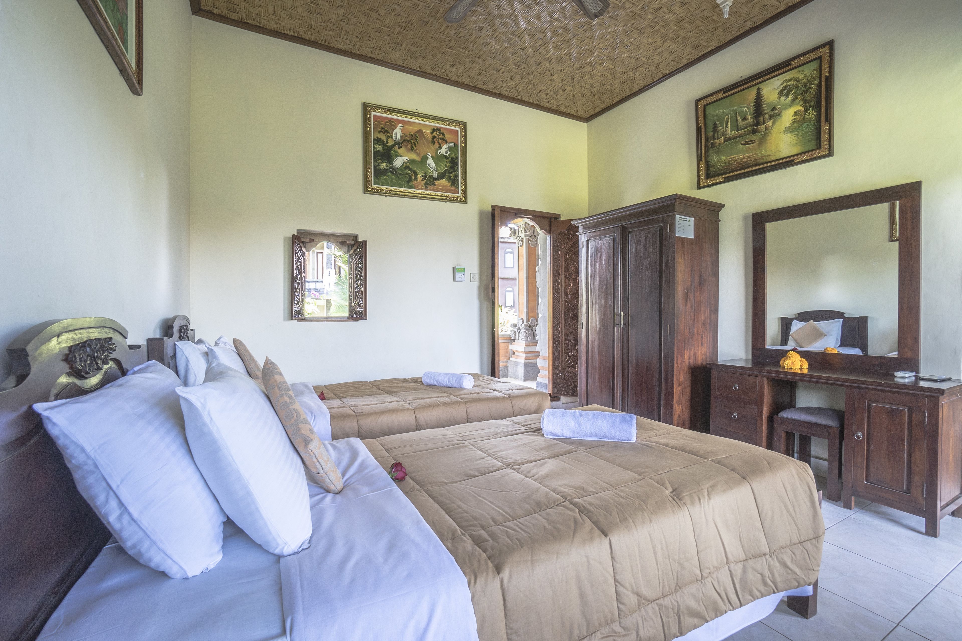 A hotel room with two beds, a wooden dresser, a mirror, and two paintings on the walls.