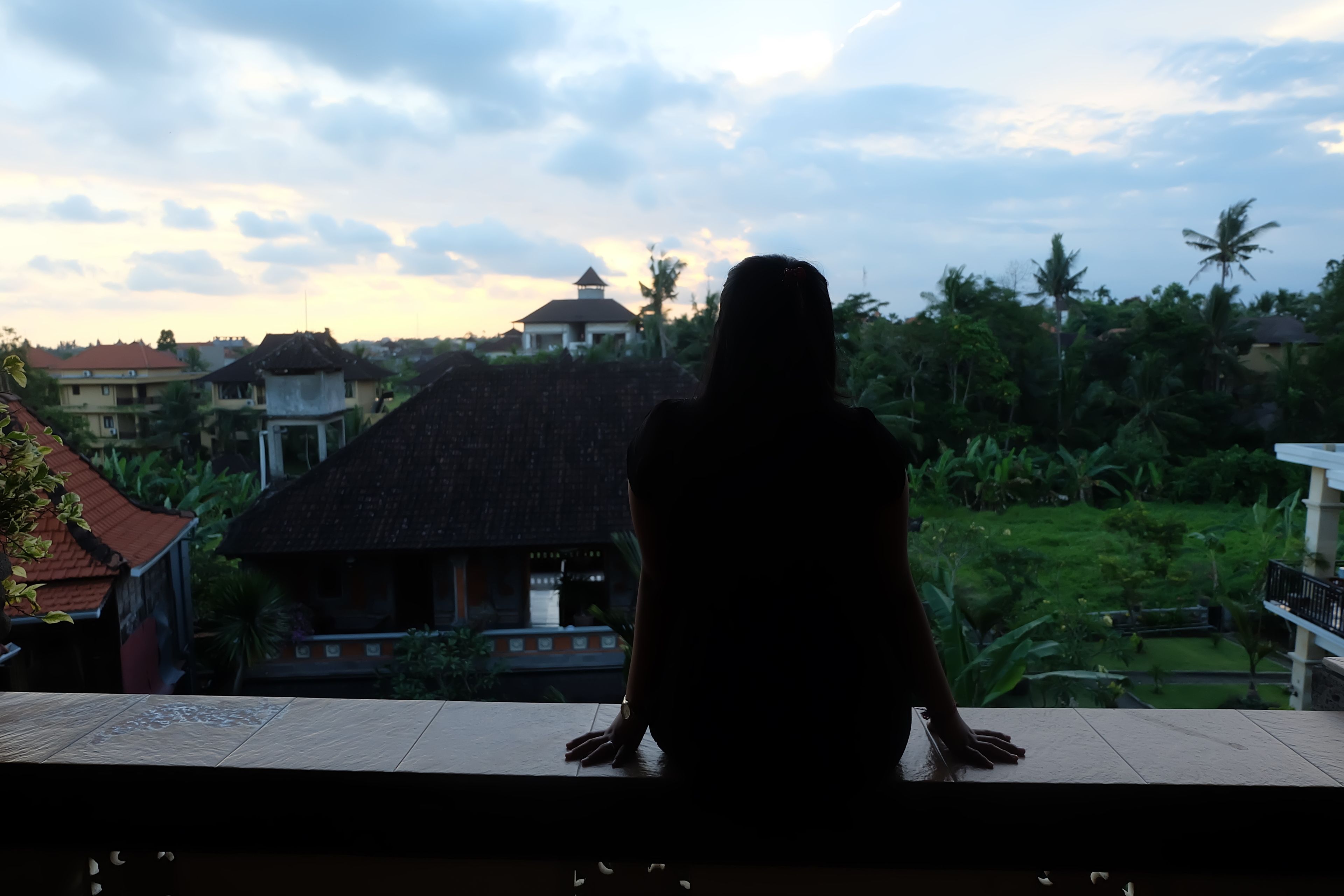 Une personne assise sur un balcon donnant sur un quartier résidentiel, avec des maisons et de la verdure.