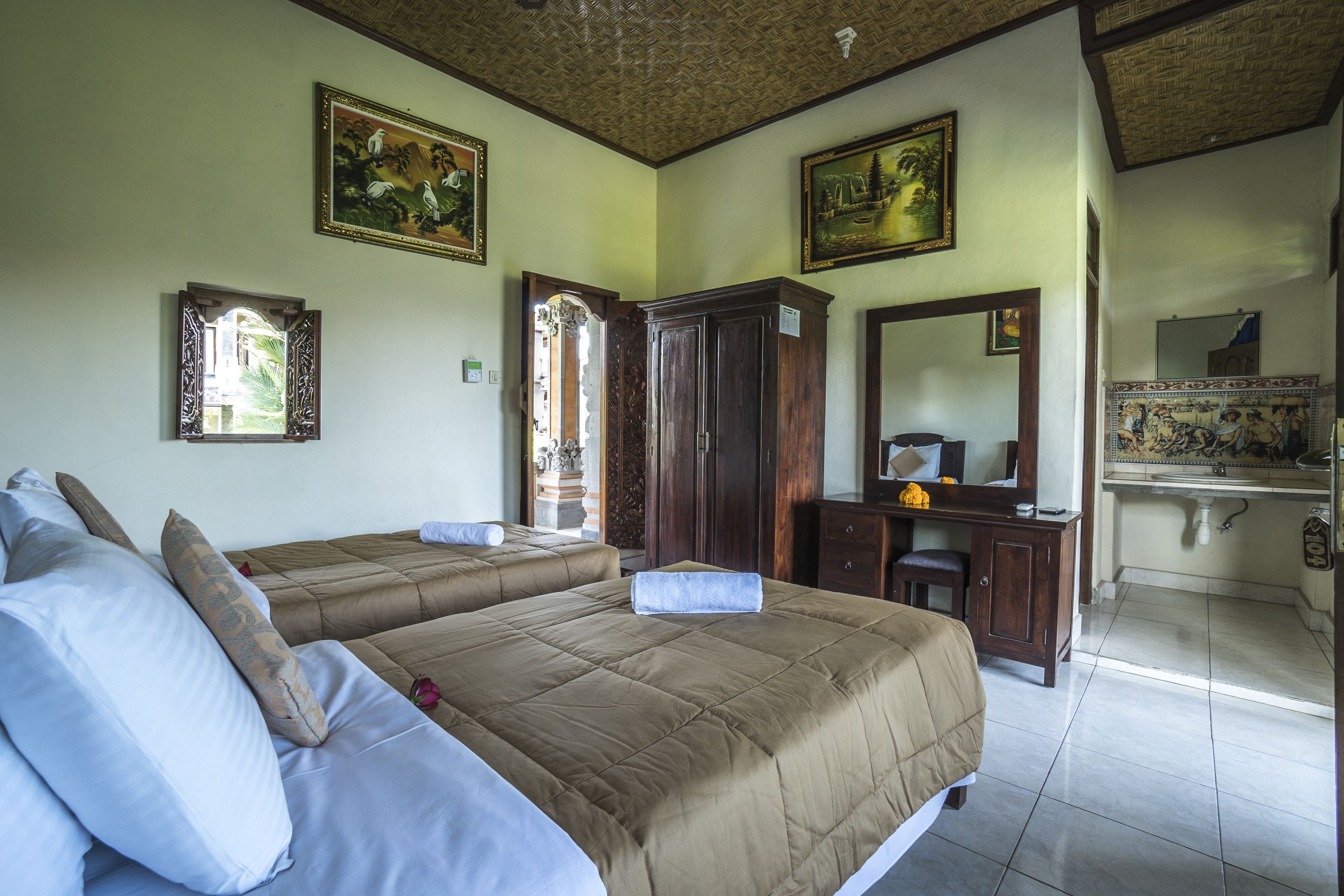 A bedroom with two beds, a wooden wardrobe, a mirror, and artwork on the walls.