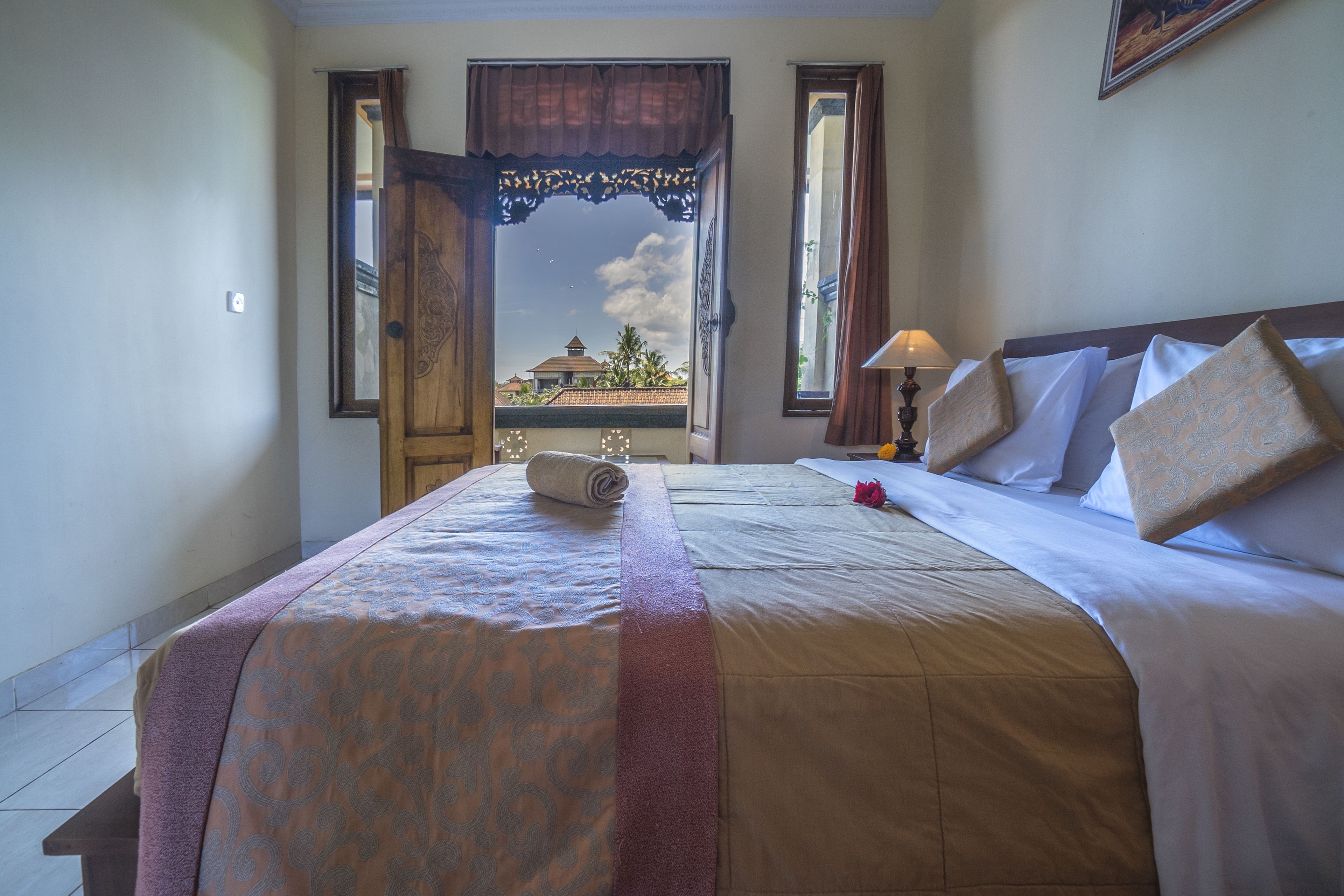 A hotel room with a large bed, a window with curtains, a view of buildings, and a lamp on the nightstand.