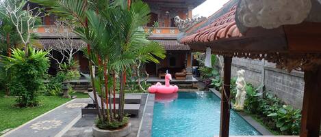 Um pátio com piscina, boia de flamingos rosa e uma estátua.