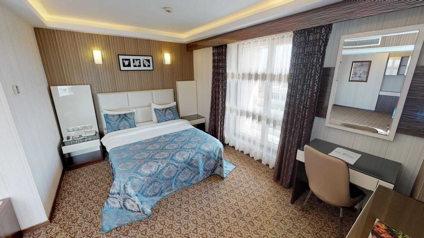 Habitación de hotel con cama, escritorio, silla, espejo y ventana con cortinas.
