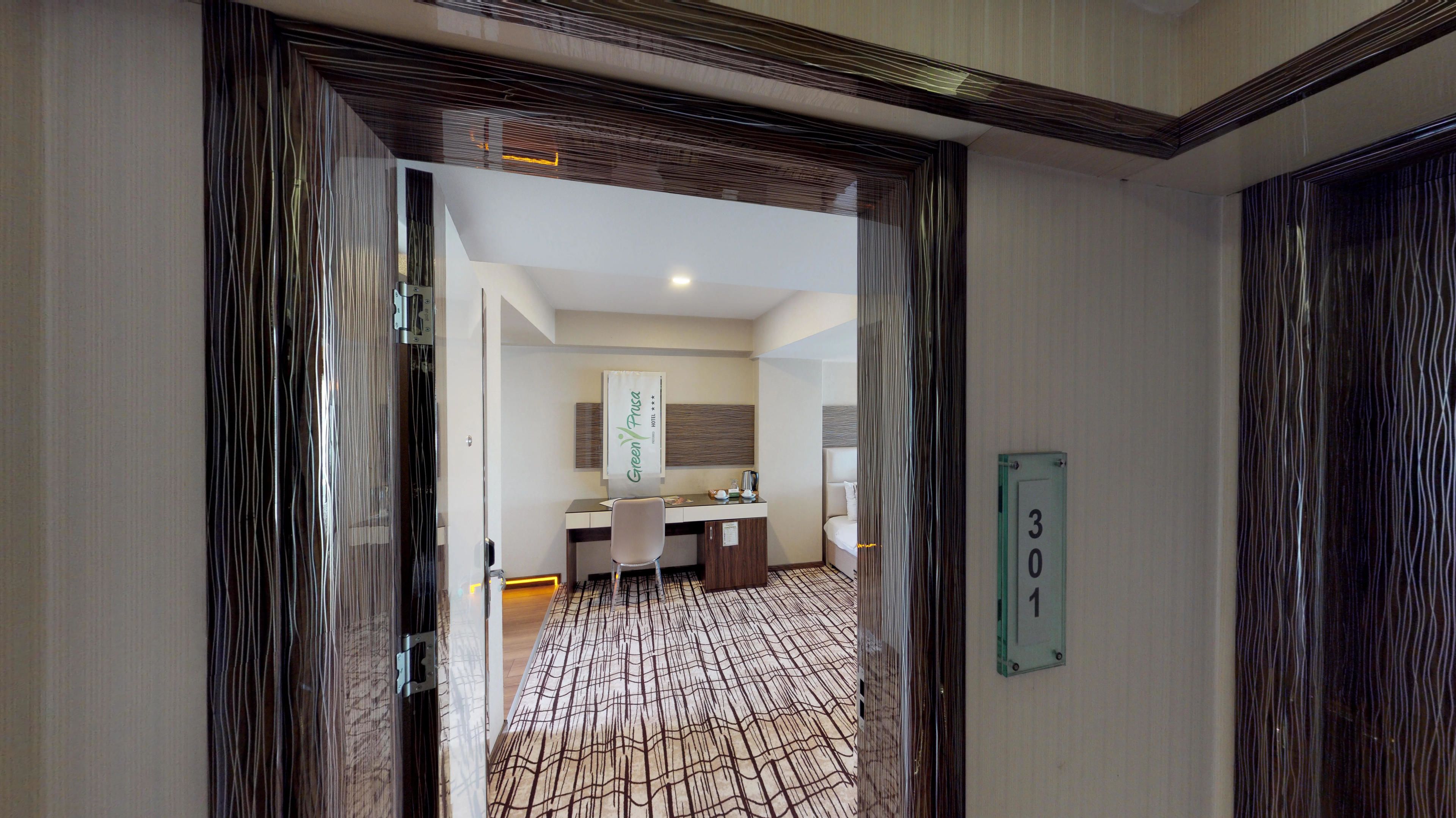 Habitación de hotel con diseño moderno, que incluye un escritorio, una silla y una cama. Se aprecia un baño con lavamanos y espejo al fondo.