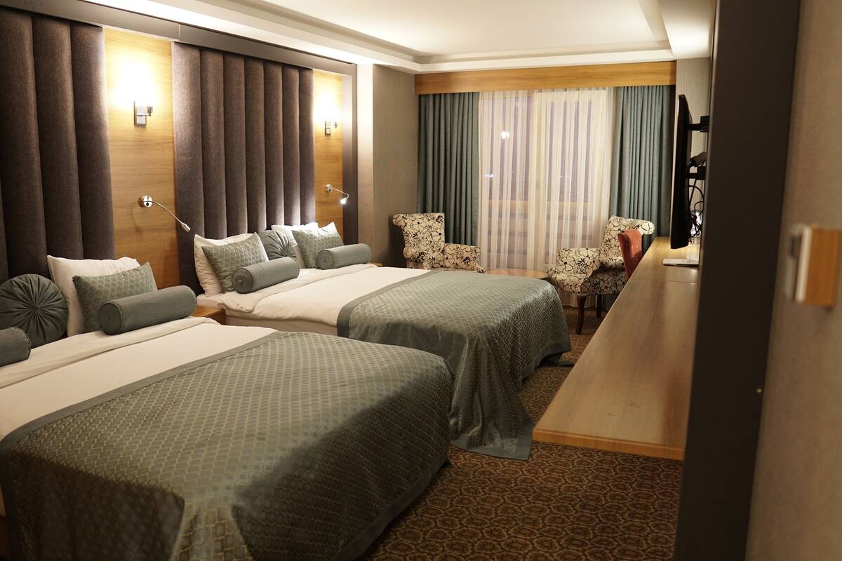 A hotel room with two beds, a desk, a chair, and a large window with curtains.