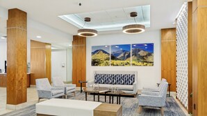 Un hall con un sofá, dos sillones, una mesa de centro, pilares de madera y una pared decorada con una pintura de un paisaje montañoso.
