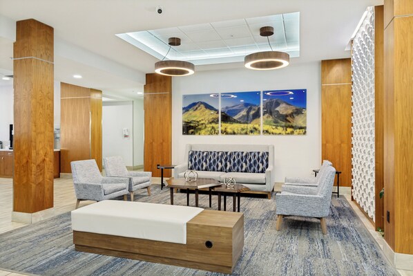 Un hall con un sofá, dos sillones, una mesa de centro, pilares de madera y una pared decorada con una pintura de un paisaje montañoso.