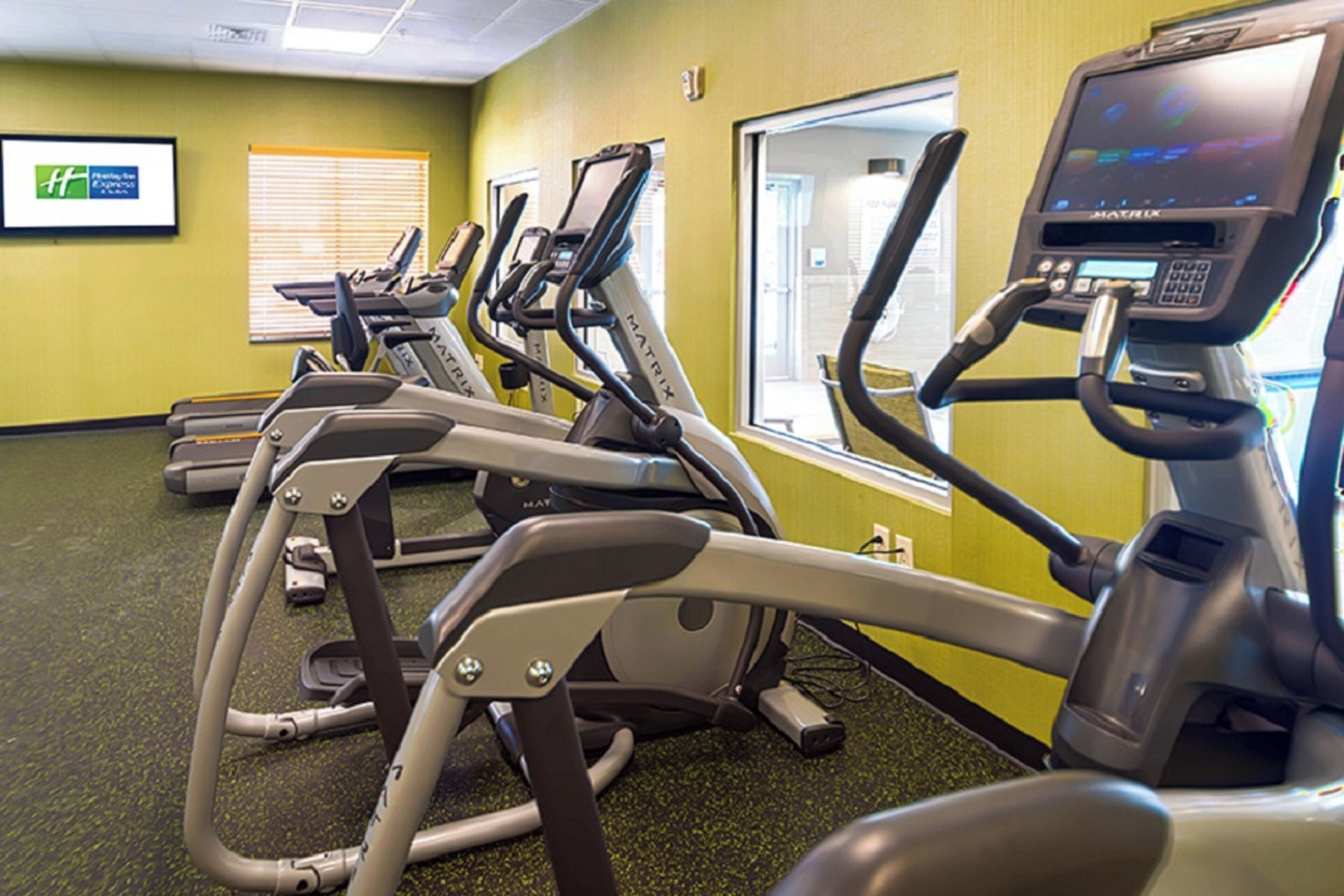 A row of stationary exercise bikes in a gym with a green wall and a window.