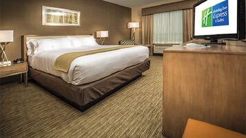 Ein Hotelzimmer mit einem großen Bett, zwei Nachttischen mit Lampen, einem Schreibtisch mit Computer und einem Fernseher, der das Holiday Inn Express Logo zeigt.