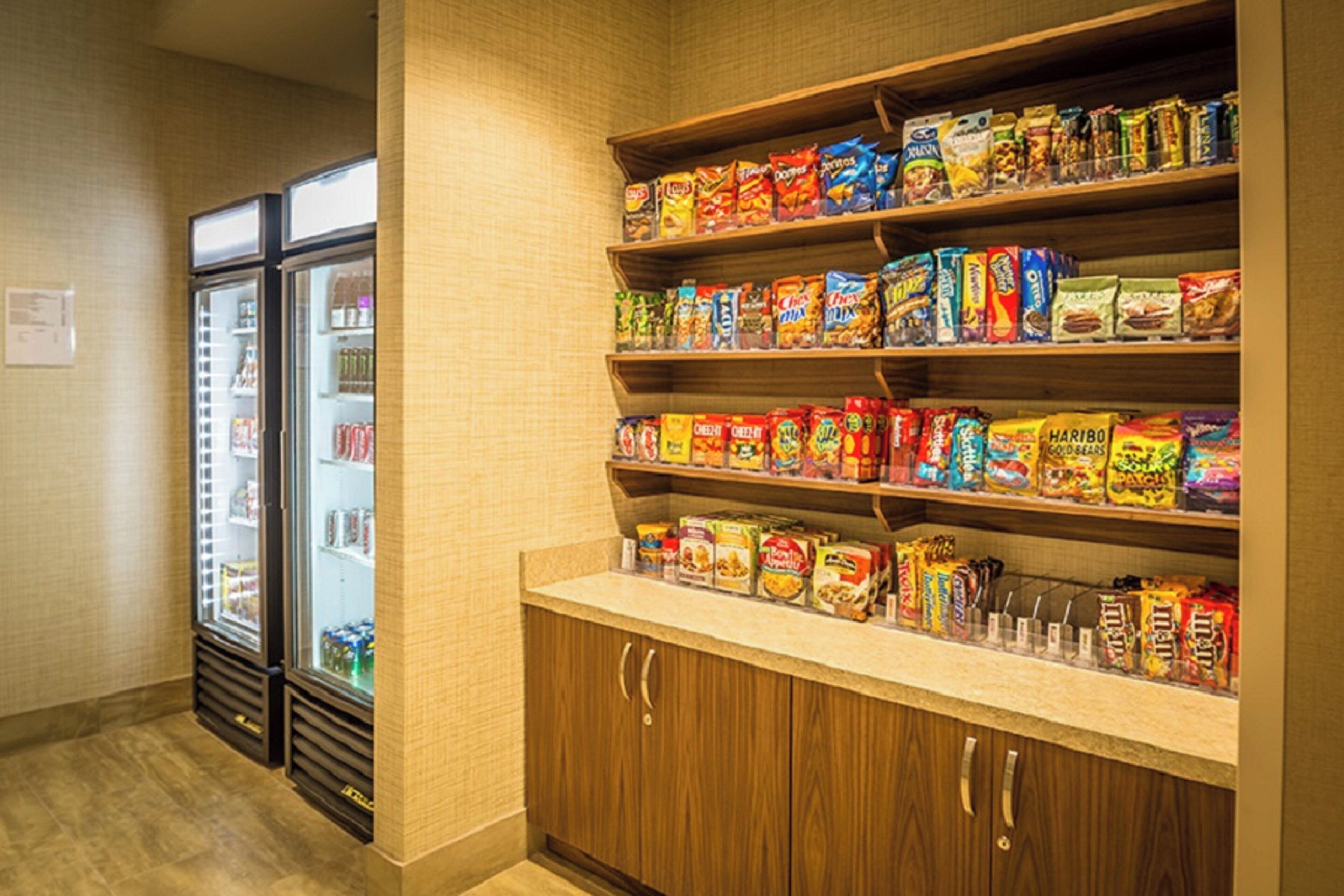 A snack bar with shelves stocked with various packaged snacks and a refrigerator in the background.