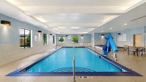 Una piscina interior con agua cristalina, una silla de salvavidas y una mesa con sillas junto a la piscina.